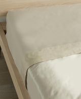 Dune-toned cotton percale flat sheet layered on a bed